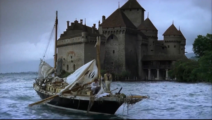 Fotograma de Remando al viento con los dos poetas en una barco destrozado por la tormenta y el Castillo de Chillon al fondo.