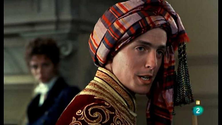 Fotograma de la película Remando al Viento con un primer plano de Hugh Grant como Lord Byron y al fondo Elizabeth Hurley como Claire Clairmont.