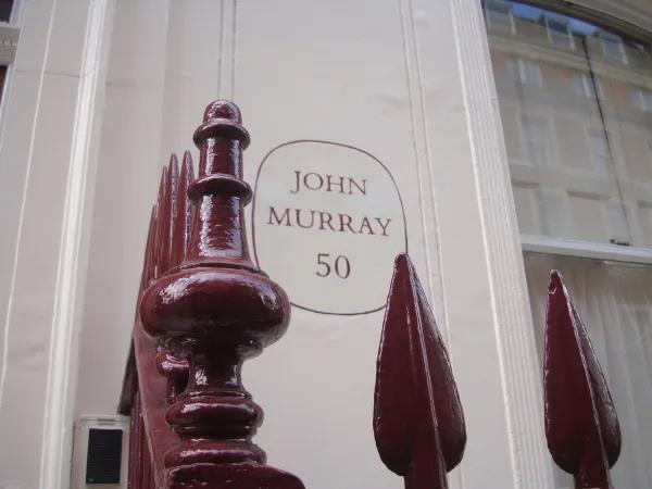Detalle de la fachada de la editorial Murray, donde detrás de una verja roja, se muestra un circulo con John Murray 50 en su interior.